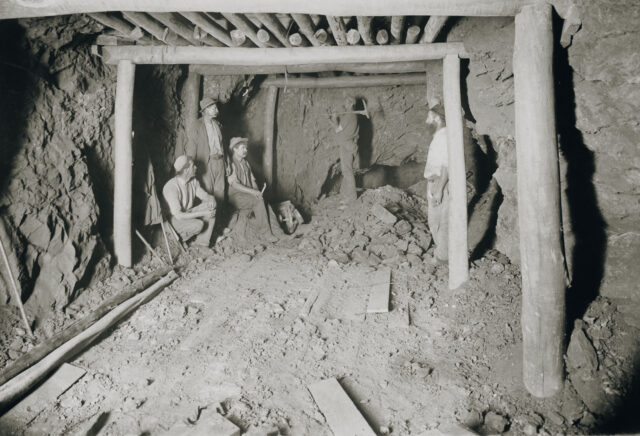 Men sitting in a mine supported by wood beams.