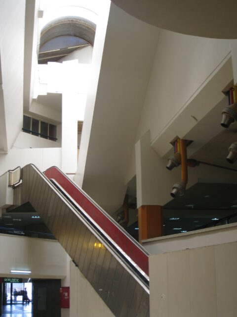 A walkway with an escalator and a keyhole to look up toward higher floors