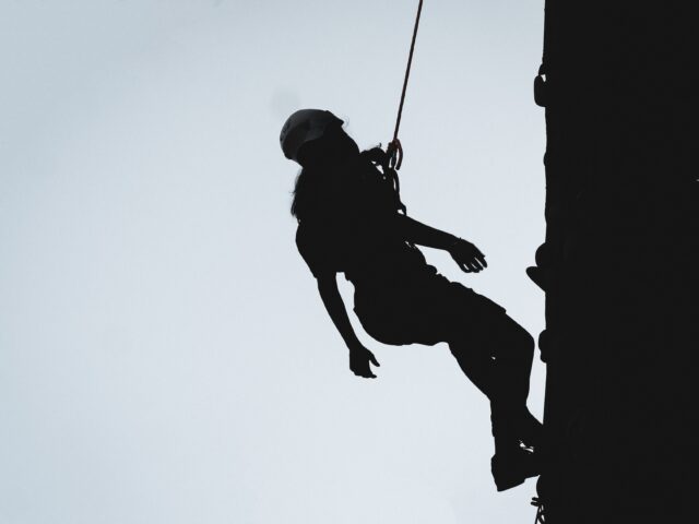 Woman climbing down a rocky ledge with a rope