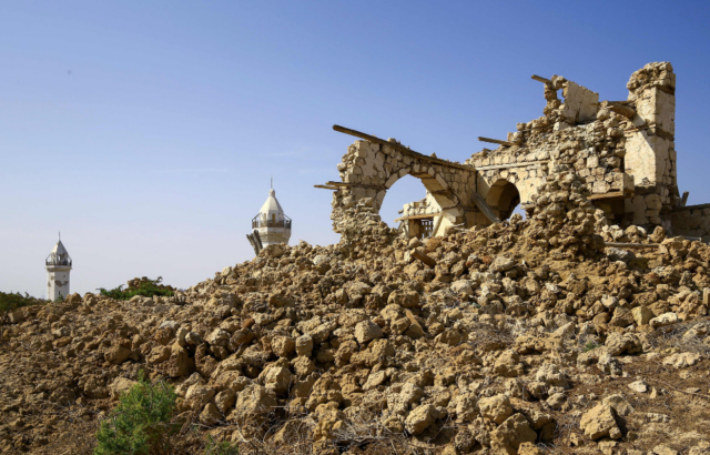 A ruined building on top of rubble, two tower tips in the background.