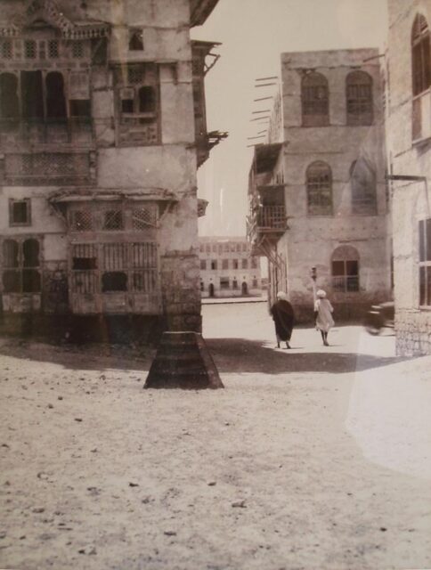 Two men walking in the street, buildings looming over them.