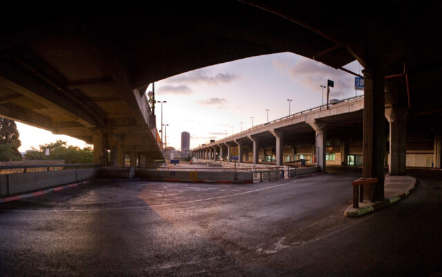 An outdoor photo of a bus station and overhead bridge.