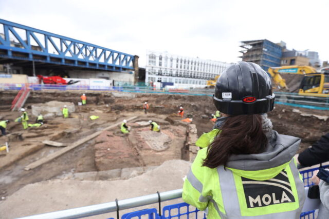 Archaeologist with the Museum of London Archaeology (MOLA) watching other archaeologists excavate the Liberty of Southwark site