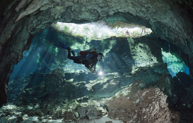 Diver underwater in a cenote with the entrance hole above his head.