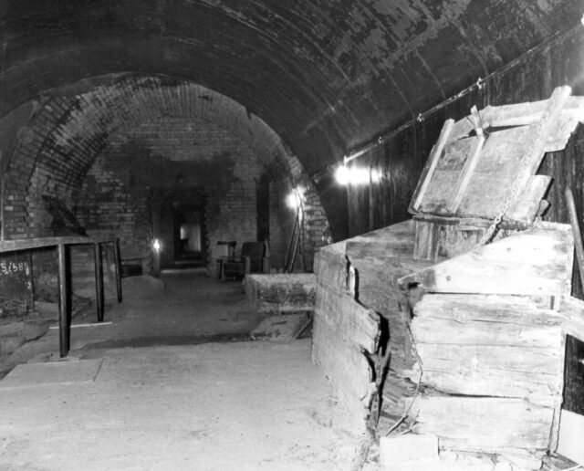 Wooden crates and tables inside an underground brick bunker.