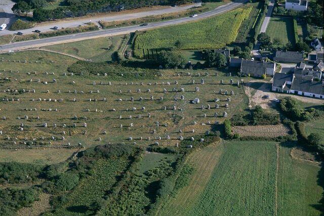 Aerial view of rows of standing stones in a field beside a house.