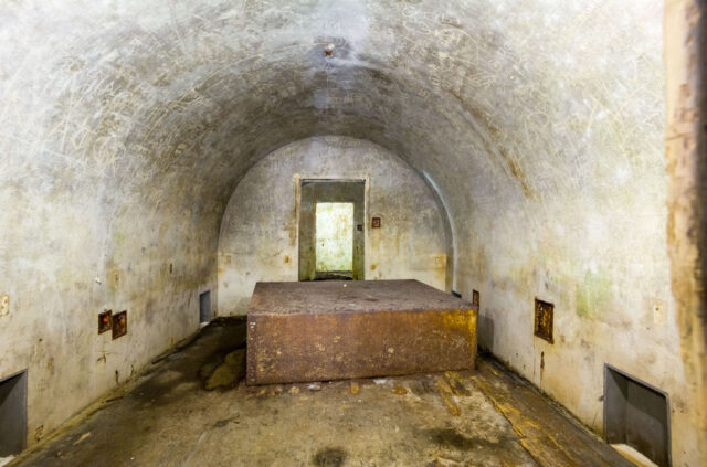 Armored cabinet on the floor of a bunker with curved walls covered in graffiti. 