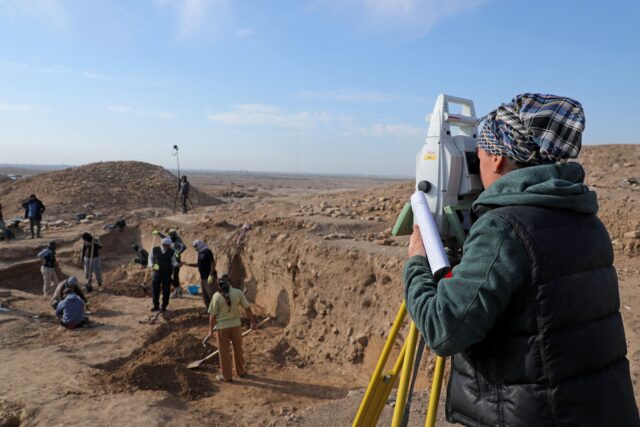 An archaeologist looking through a tool at the dig site.