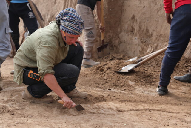 An archaeologist using a tool on the ground of a dig site.