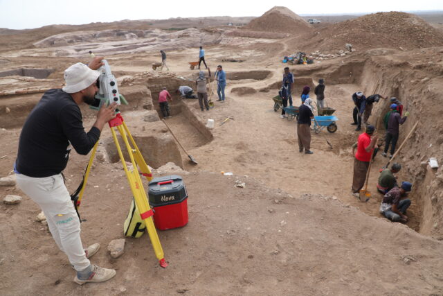 Archaeologists working at a dig site, a man looking through a tool. 