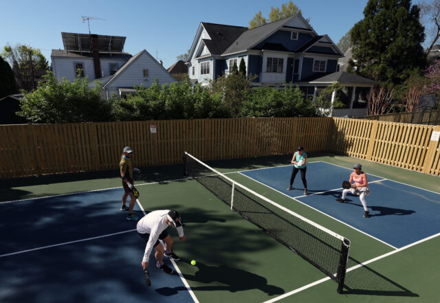 Four people playing pickleball on a court behind some houses.