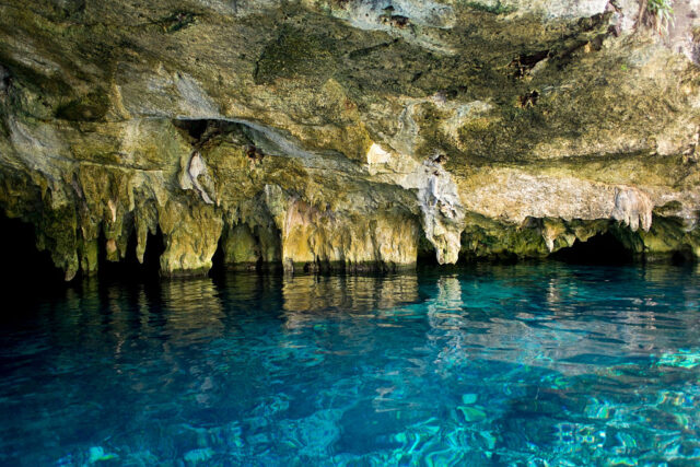 Interior of a cenote with rock walls and clear blue water throughout.