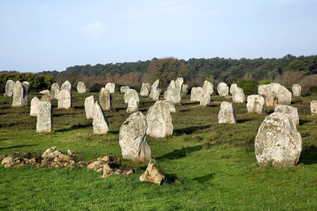 View looking out at a field full of standing stones on green grass with blue sky behind them.