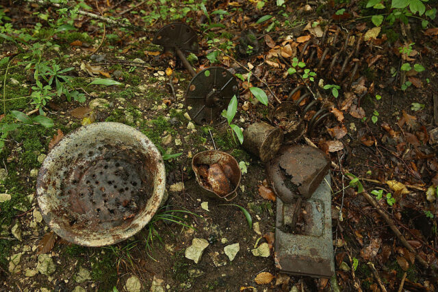 Bowl, artillery springs, a metal lid and a spool for communications wire strewn on the forest floor
