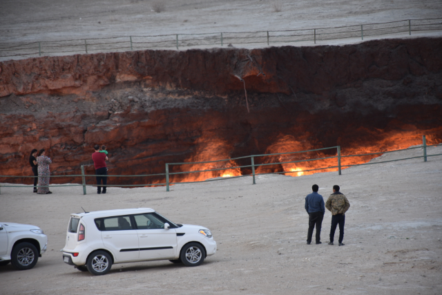 People and cars surrounding Turkmenistan's Gates of Hell that has been fenced off.