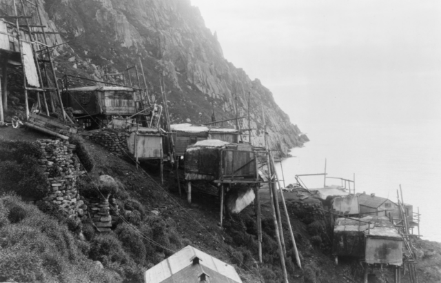 Side view of houses on stilts along a cliff face.