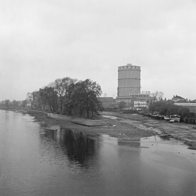 View of the Thames river, with boats grounded upon the bank and a tower in the background.