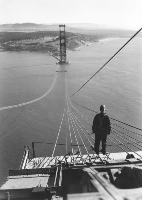 A man stands on the cables of the Golden Gate Bridge during its construction.
