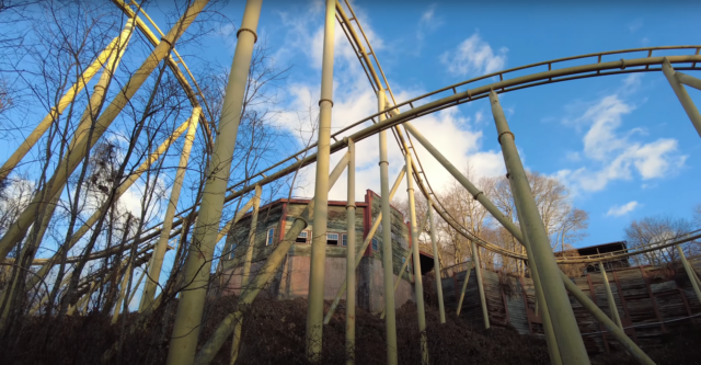 The frame of a rollercoaster flanked by a building with boarded up windows.