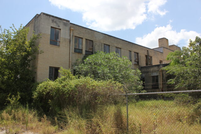 View of an abandoned building surrounded by bushes.