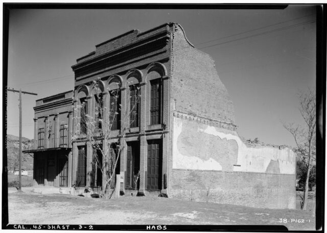 Two brick buildings side-by-side. One is severely destroyed at the back.