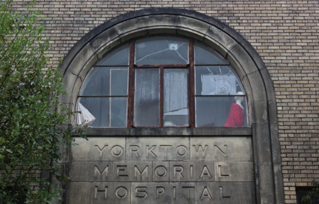 A damaged window above the stone sign of the Yorktown Memorial Hospital.