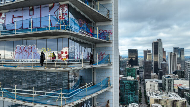Graffiti artists walking the unfinished balconies of a skyscraper, graffiti on its windows.