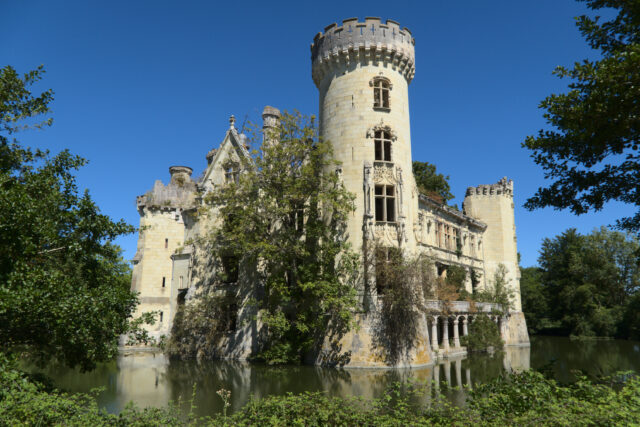 An abandoned chateau with bushes growing up its side.