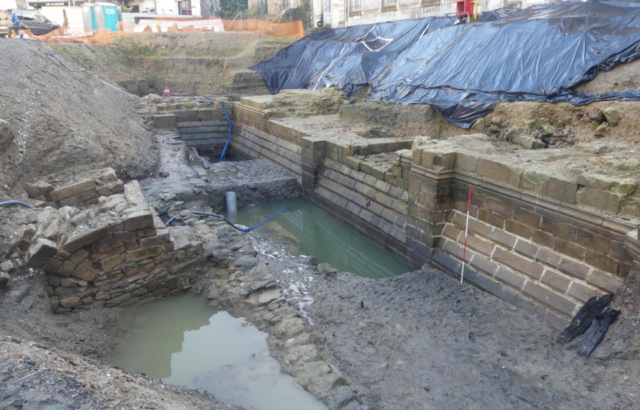 An archaeological dig site with a moat and exposed stone walls.