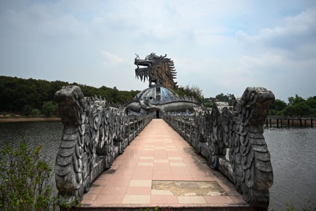 View down a boardwalk toward a dragon-shaped aquarium at Hồ Thuỷ Tiên waterpark