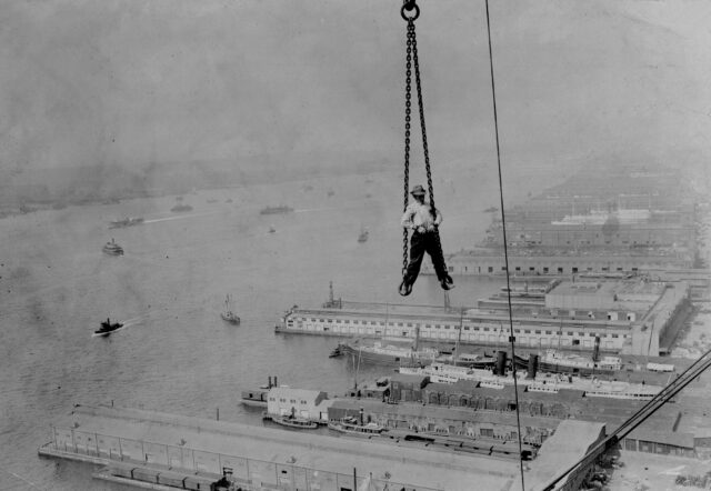 A worker rides a chain on a crane.