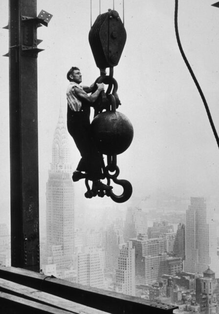 A man rides a crane hook in the sky.