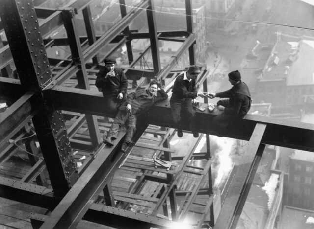 Construction workers having lunch on a steel girder, one laying down.