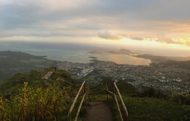 View of descending stairs at the top of a mountain in Hawaii. A cityscape beyond it.